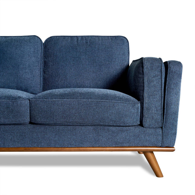 The Maddox is a blue mid-century modern sofa with two seat cushions and a wooden frame, ideal for enhancing your living room. The right armrest and half of the sectional stand out against a white background.