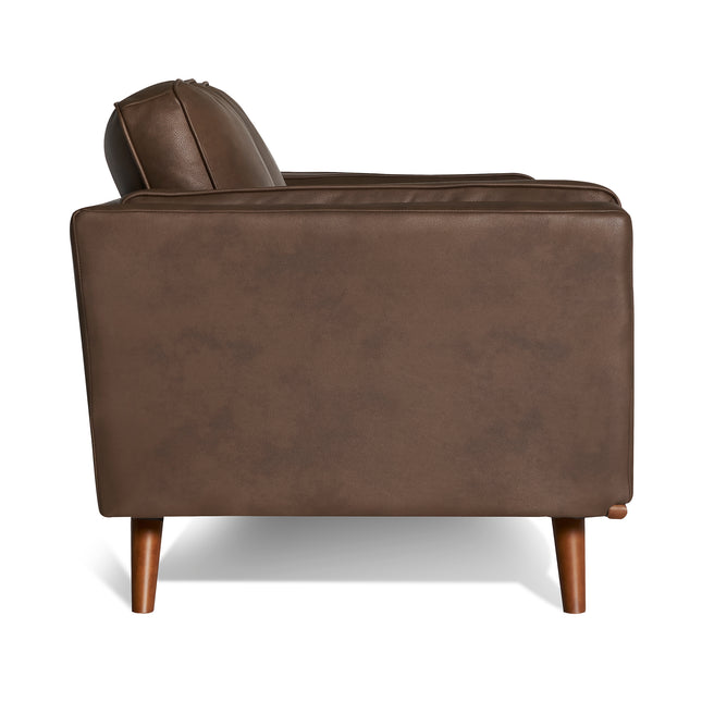A side view of the Maddox Loveseat, a mid-century modern brown leather sofa with wooden legs, is captured against a plain white background. It features a boxy shape with plush backrest cushions, providing both style and comfort.