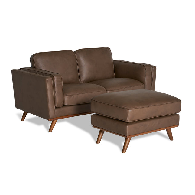 The Maddox Loveseat is a brown leather, mid-century modern piece with angled wooden legs and plush cushions. It includes a matching rectangular ottoman, two removable cushions, and sleek armrests that enhance its contemporary look.