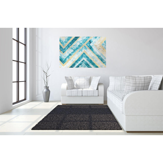 A minimalist living room showcases a white sofa with plaid cushions on a gray rug over light wood floors. The Abstract Chevron artwork boasts blue and gold geometric patterns on the wall. A tall plant by the large window enhances the spaces charm.