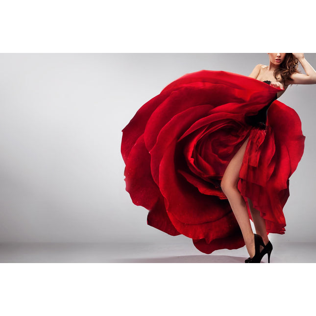 A woman poses in a dramatic Rosie Leg red gown resembling a giant rose, with one leg exposed. She wears black high heels against a gray background. The dresss voluminous petals create an artwork with striking visual effects, leaving a lasting impression.