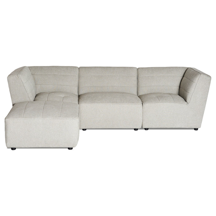 The Millenium 3 Piece + Ottoman is a light gray, L-shaped modular sectional sofa that features clean lines, tufted cushions for plush comfort, low black feet, and offers ample seating with a touch of modern luxury.