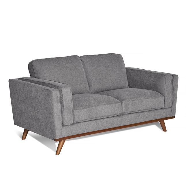 The Maddox Loveseat is a modern, grey piece showcasing square armrests and plush cushions. Its wooden legs angle outward, embodying a minimalist, mid-century modern design ideal for a stylish living room.