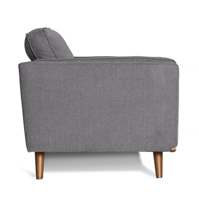 Side view of the Maddox Loveseat in gray upholstery with wooden legs against a white background; it showcases plush cushions and a boxy design, merging mid-century modern style with a cushioned seat for a sleek and minimalist appearance.