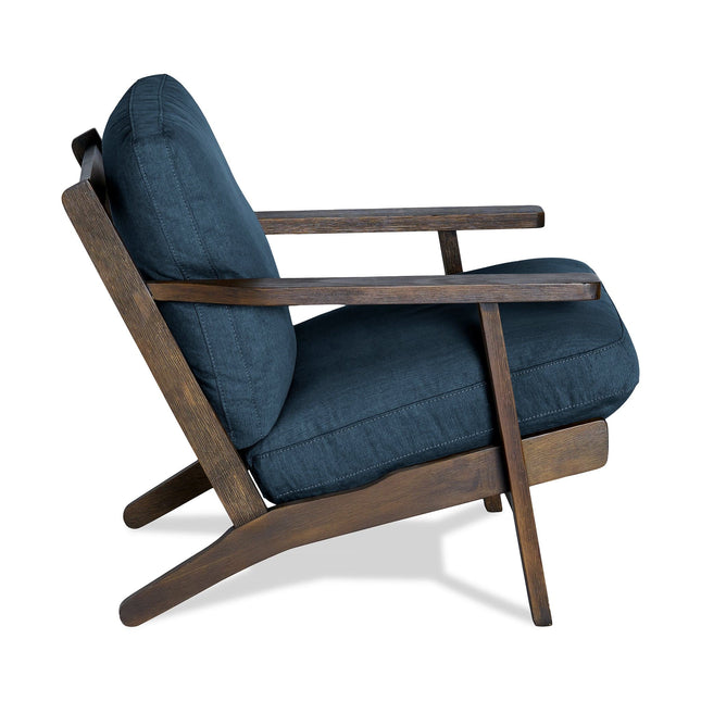 The Peyton Chair is a mid-century modern armchair featuring a dark wooden frame and navy cushions. It has a slanted seat and backrest, with elegant armrests that diagonally extend downward, offering both style and comfort in its angular design.